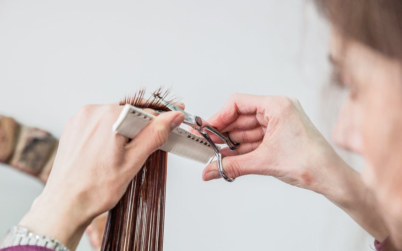 Stylist cutting a section of brown hair with scissors and a comb