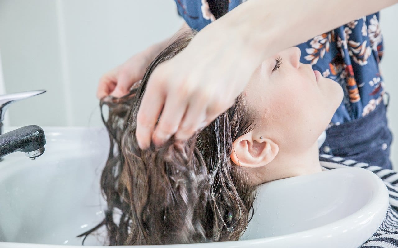 Stylist massaging shampoo into a client's wet hair at the basin
