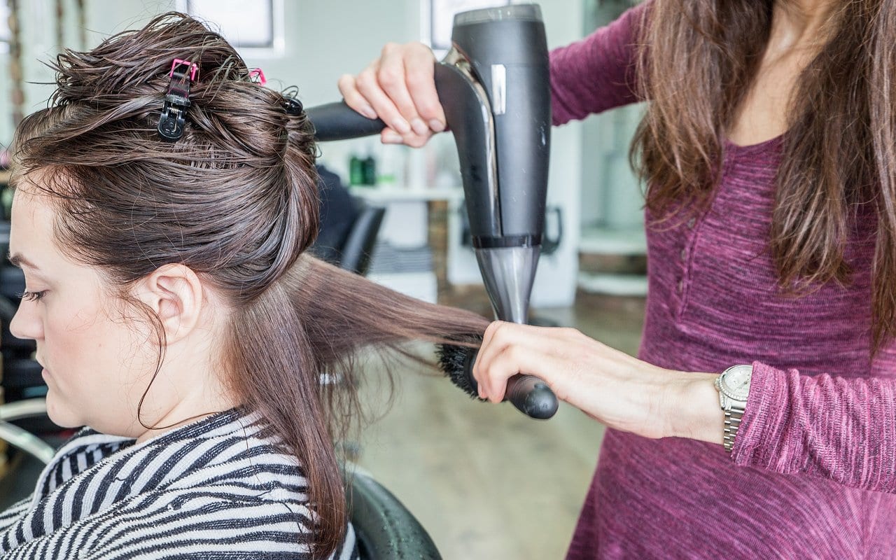 Stylist blow-drying and brushing a client's long brown hair